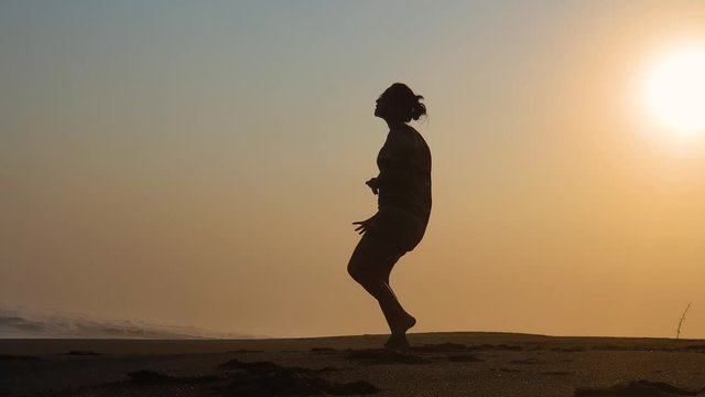 Silhouette of young woman dancing on the beach at sunset time. Shot in 4k resolution