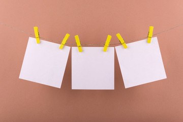 white sheets of notepad for notes and reminders of white color fastened with decorative yellow clothespins hang on a rope on a brown background