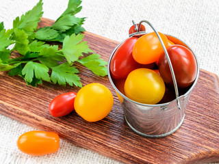 Ripe multicolored mini tomatoes in a small zinc or metal bucket and parsley on a brown wooden cutting board. Vegetables, vegetarian and healthy eating.
