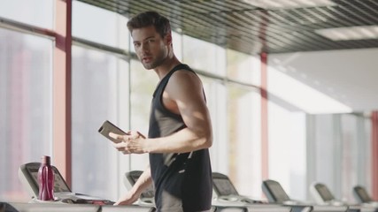 Athlete man talking cellphone on treadmill in fitness club.