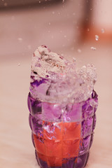Frozen moment. Close-up of a splash of water in a purple glass with a blurred background