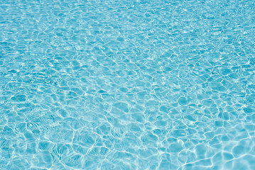 Background of water in blue swimming pool, water surface with a sun reflection