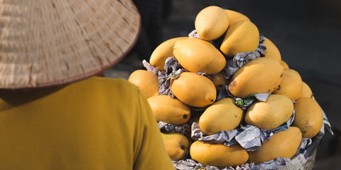 Street vendor in a conical hat sells mango at market in Ho Chi Minh City, Vietnam