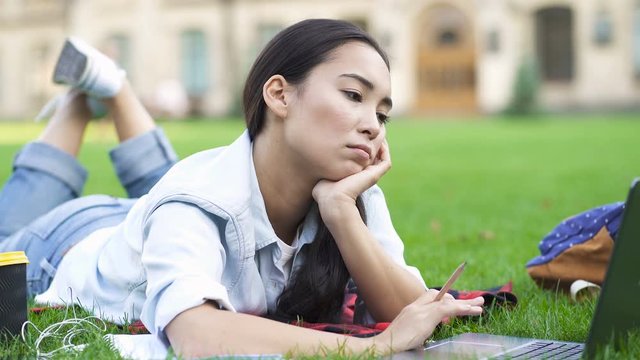 Tired student girl working with notebook computer. Lying on the grass in the park.