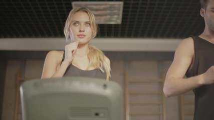 Concentrated sport couple talking in gym. Closeup couple running on treadmill