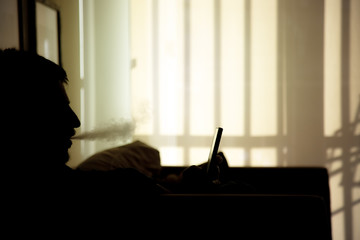 Silhouette of man throwing smoke with a vaporizer while writing with his smartphone