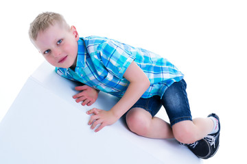 A beautiful little boy is photographed near a white cube. The co
