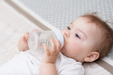 Little girl with a bottle in her hands and a pacifier in her mouth