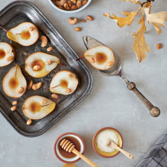 Flat lay with a tray of baked pears with caramelized nuts on gra