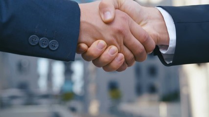 Two business partner shake hands when meeting. Close-up of a handshake of two successful businessmen making a deal. Slow motion, unrecognizable person