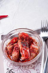spicy marinated herring  fillet in transporant bowl with red pepper, fresh chili  and seasonings. served at white table. close up. copy space