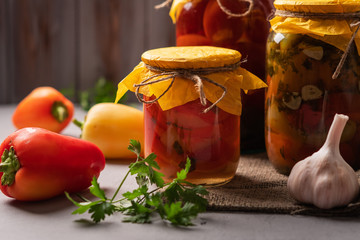 Homemade jars of pickled peppers and tomatoes on a rustic wooden background. Pickled and canned...