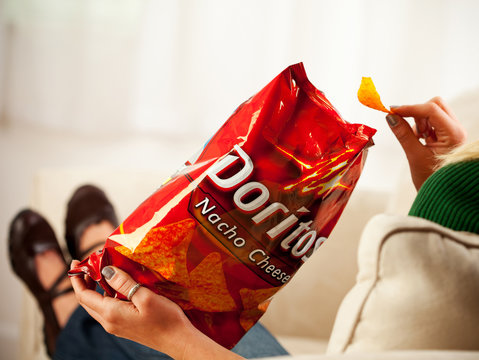 Woman Eats Chip From Bag Of Doritos, Produced By The Frito Lay Company.