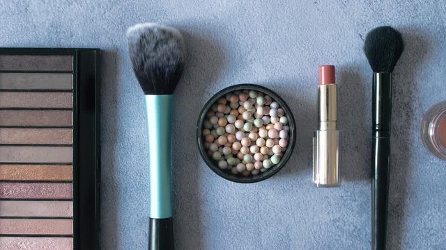 Top view of cosmetics ads with lipstick powder and brushes on stone texture background. Make up women powder balls. 4k footage.