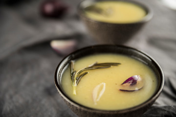 Сream soup with rosemary, potatoes and onions in brown soup plates.