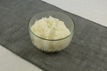 Warm steamed white rice in glass bowl with condensation from heat placed on woven runner fabric on white tablecloth