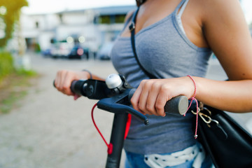 Close up on midsection of young woman holding steering column handle grip of electric kick scooter on the street in summer day