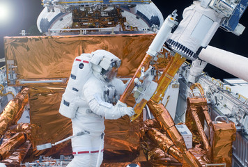 The astronaut in a space suit, in an outer space, is engaged in repair of the space station. ...