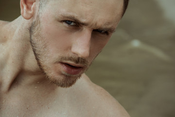 Obraz premium Strong face male model on the nature background with sand and water on the beach on the sunset