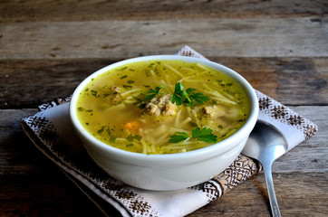 Homemade soup with meatballs and noodles, folk napkin on a wooden table.