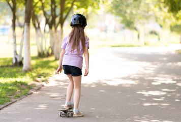 A little girl is riding a skateboard from the back.