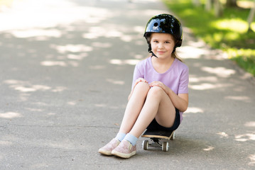 Little girl in a helmet sitting on a skateboard.