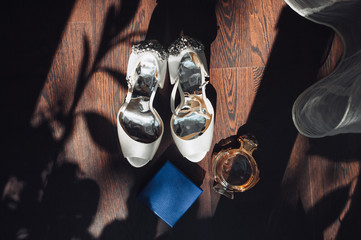 Morning of the bride. Wedding details. Shoes, perfume and box are on the background of the parquet,...