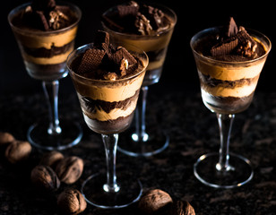Close-up of traditional coffe cream dessert with an interspersed chocolate crunch served in glass cups with a black background and a marble table.