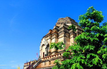 The old pagoda built from brown bricks in Thailand at the top has disappeared, is located in a temple area with trees on the side in the daytime and behind the sky.