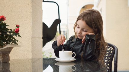 Stylish little schoolgirl enjoys delicious coffee on the summer terrace of the restaurant. Coffee...