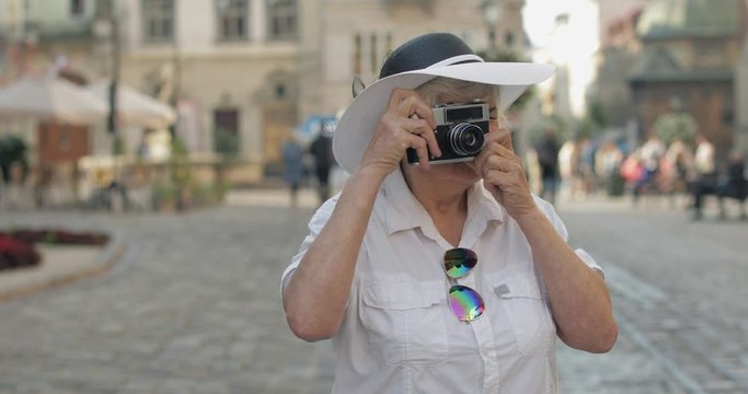 Senior female tourist exploring town and makes a photo with retro photo camera