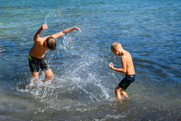 2 young naughty blonde haired Caucasian boys on their summer holiday playing in the water on the...