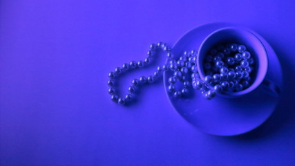 Cup of pearl necklace below neon light. With copy space to insert text. Wide screen view. It represents youth which works and have to be profitable