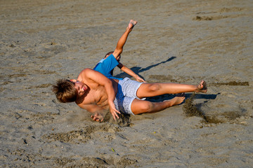 Action photo of 2 young naughty boys on their summer holiday playing fighting on the sandy beach