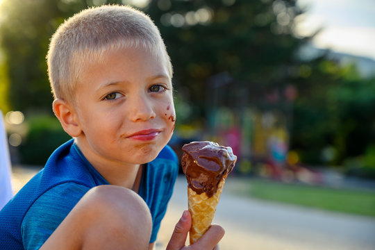 Bright summer portrait of a 6 years old naughty blonde haired Caucasian boy eating ice cream