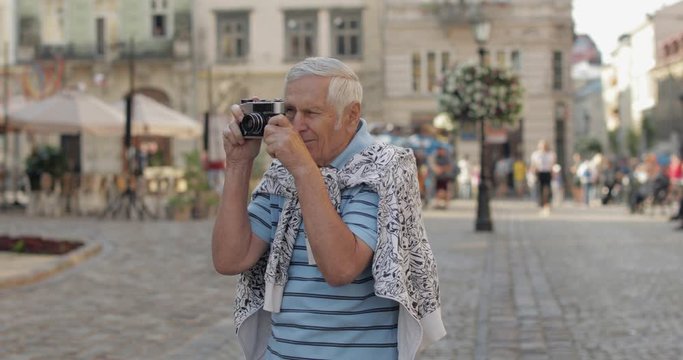 Senior male tourist exploring town and makes a photo with retro photo camera
