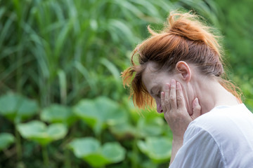 An unhappy woman holds her hands in front of her face. She is sitting in a park. Concept burnout...