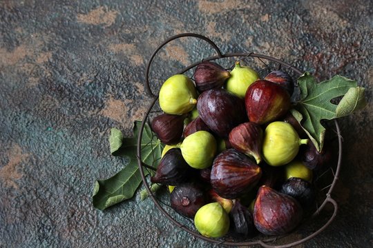 Different sorts of figs in a basket on a dark background. Large, small purple figs and white figs. Top view