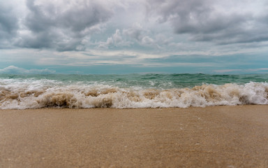 Low angle view of waves washing up onto sandy beach with dramatic overcast sky above