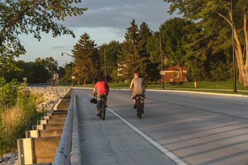 Naklejka premium Sporty company friends on bicycles outdoors against sunset cyclist going along shoreline coast Reflection sun on water Sport in Nature background 