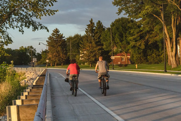 Fototapeta premium Sporty company friends on bicycles outdoors against sunset cyclist going along shoreline coast Reflection sun on water Sport in Nature background 