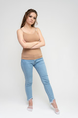 Photo full-length portrait of a pretty brunette woman girl with long beautiful curly hair on a white background in a t-shirt and blue jeans. Talking while standing in front of the camera.