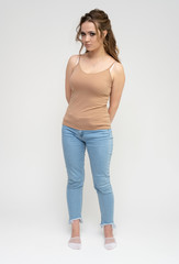 Photo full-length portrait of a pretty brunette woman girl with long beautiful curly hair on a white background in a t-shirt and blue jeans. Talking while standing in front of the camera.