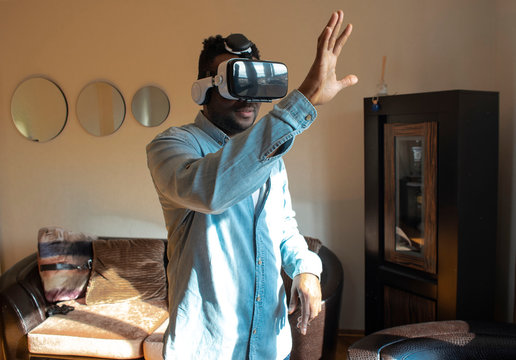 Cool handsome african american man first time wearing virtual reality glasses at home. A man is looking for bright impressions using gadgets. - Powered by Adobe