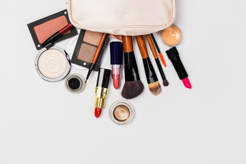 A pink makeup bag with cosmetic beauty products spilling out on to a light  background, with empty space at side