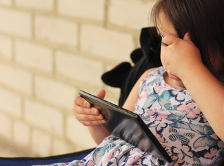 little girl in a colorful dress with a tablet against a brick wall