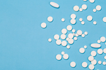 White Pills are scattered over a blue background. Close up. Medical background.