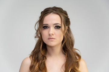Naklejka premium Close-up photo portrait of a pretty brunette woman girl with long beautiful curly hair on a white background. Standing in front of the camera