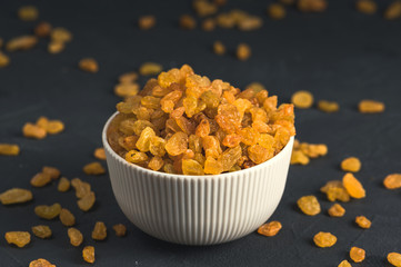 Bowl of yellow raisins on dark background