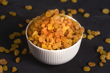 Bowl of yellow raisins on dark background